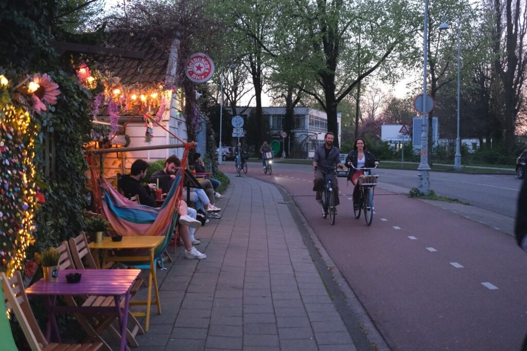 Cyclists passing a colourful hammock cafe at dusk in Amsterdam