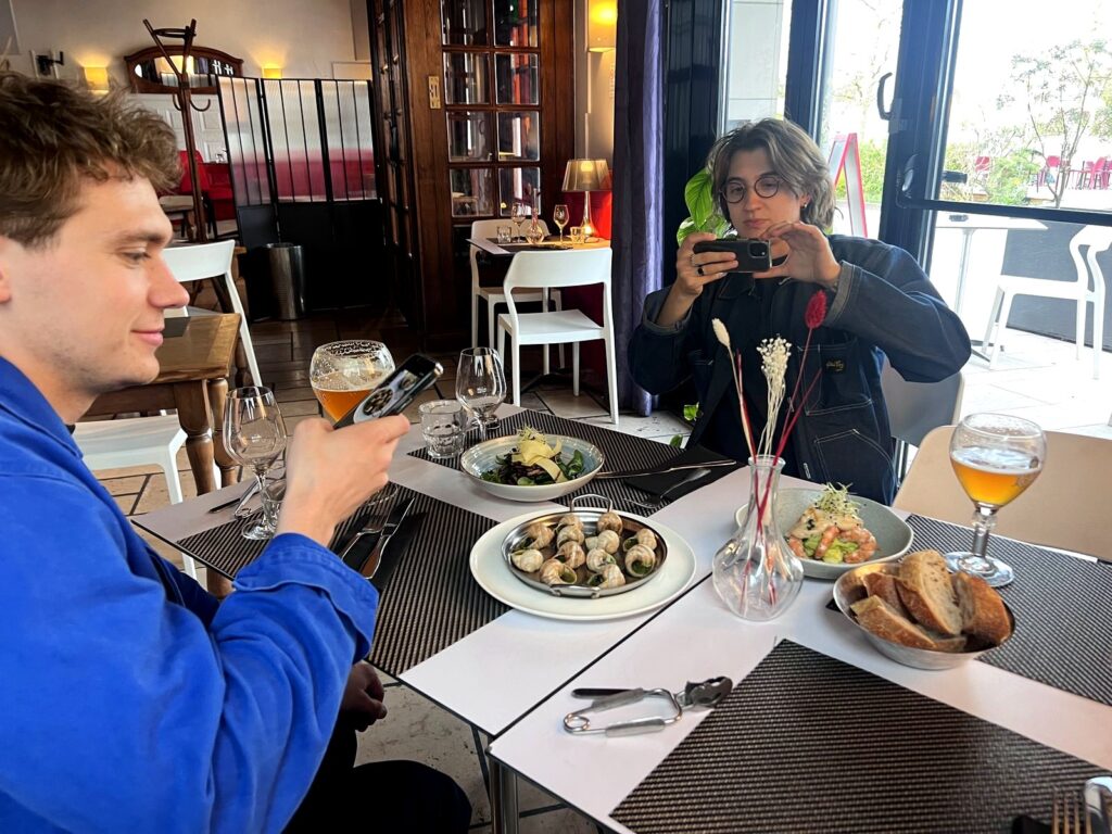 Two crew members photographing a plate of escargots at a French restaurant