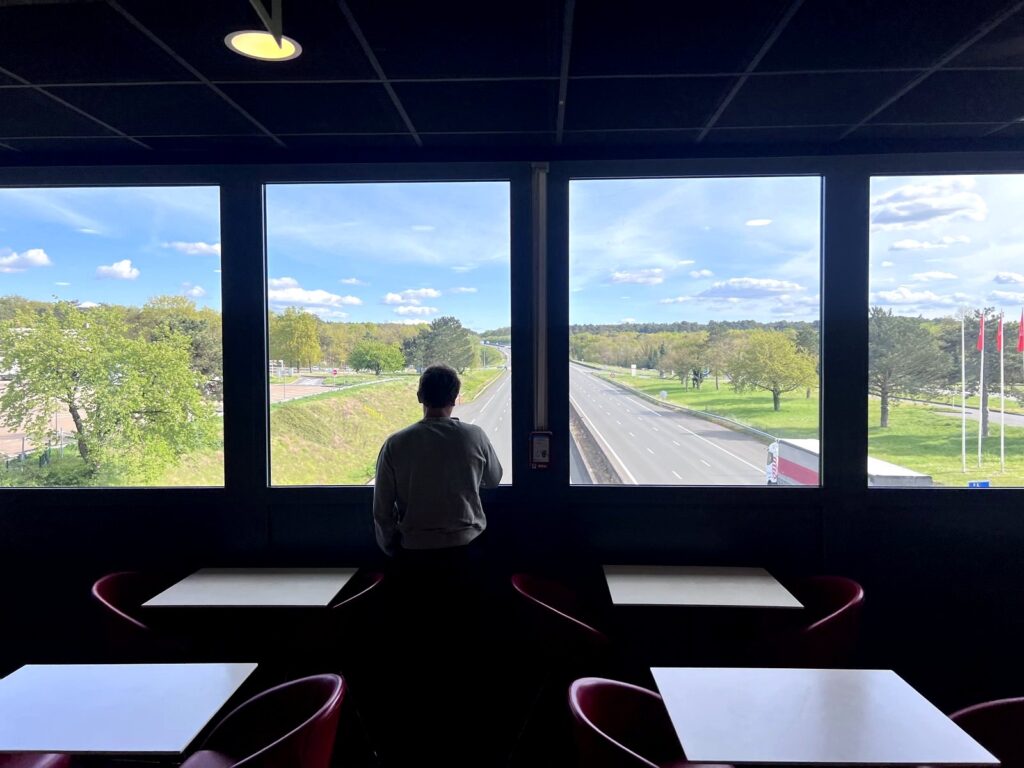 Crew member silhouetted at an autoroute rest stop window overlooking the French highway