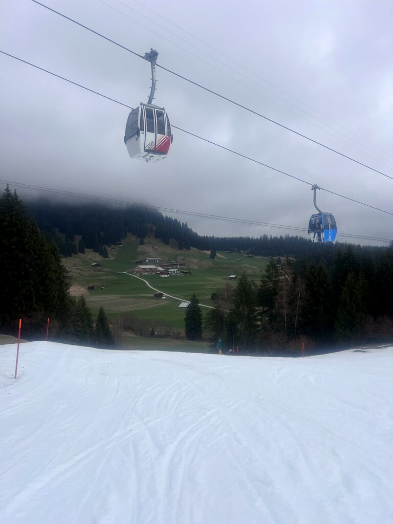 Gondolas over green fields and melting snow in Laax