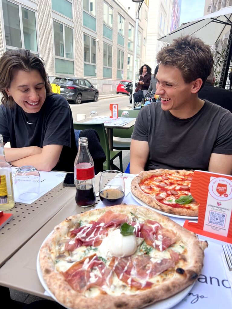 Two Arc Media crew members laughing over pizzas in Milan