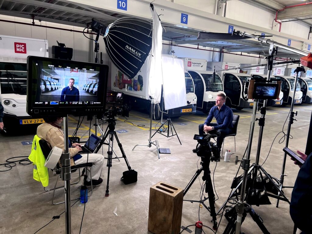 Interview setup at the Picnic depot in Amsterdam with rows of electric delivery trucks behind the subject