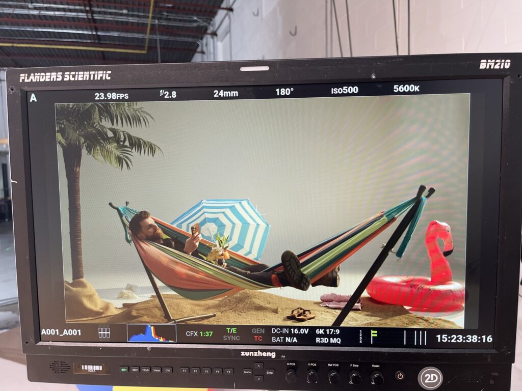 Production monitor showing the framed beach scene with umbrella and flamingo floatie