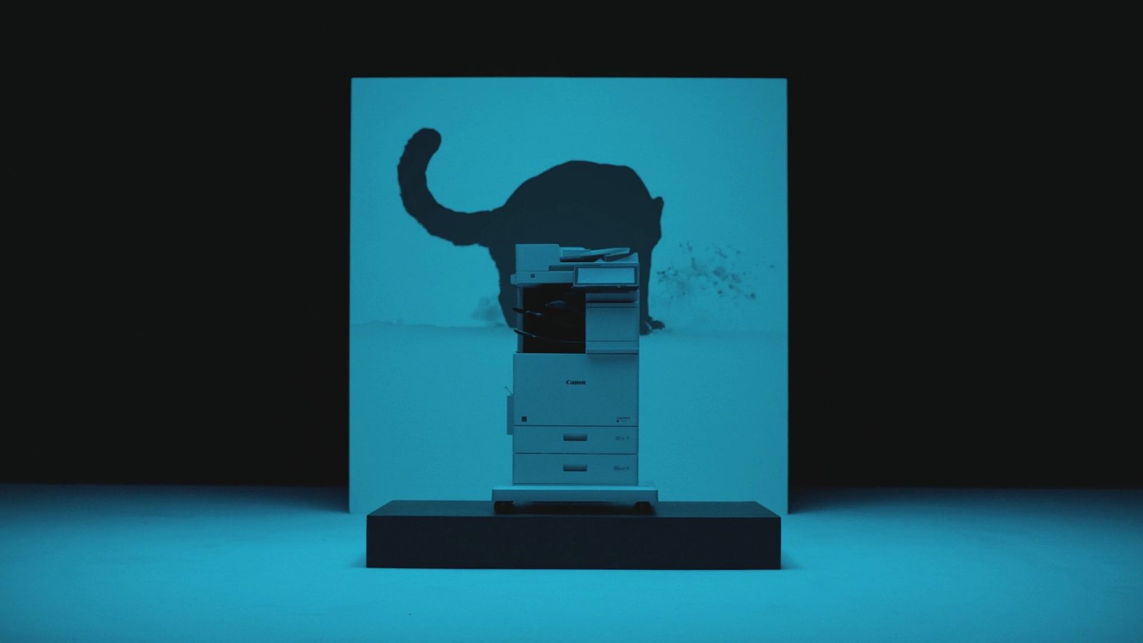A Canon imageFORCE printer lit in cyan, casting the shadow of a leaping big cat