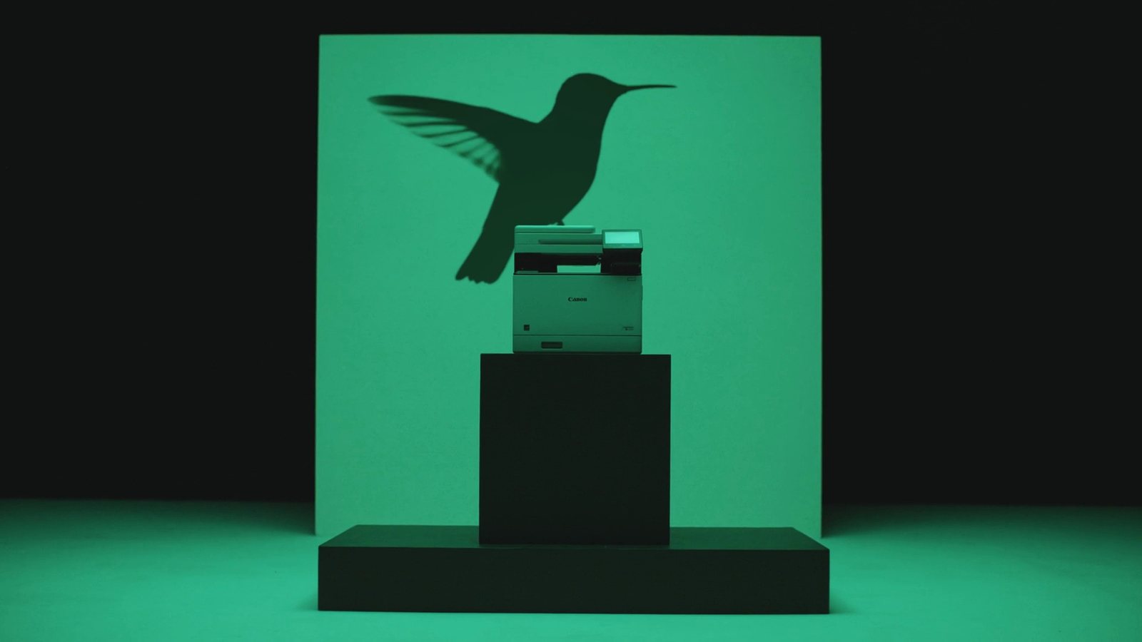 A Canon imageFORCE printer lit in green, casting the shadow of a hummingbird