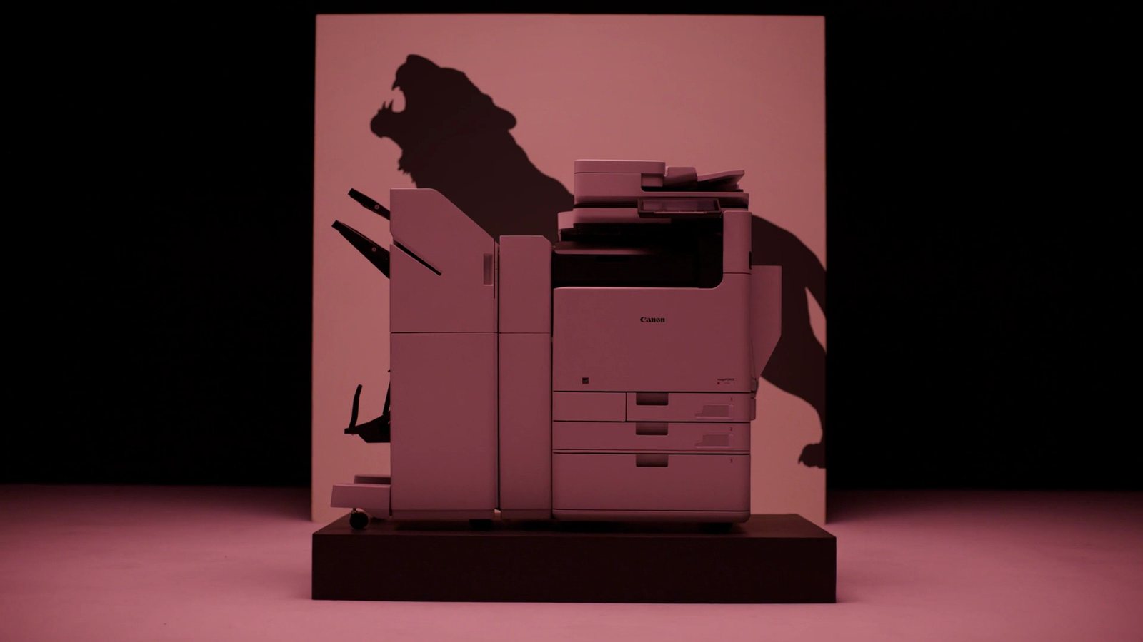 A Canon imageFORCE printer lit in pink, casting the shadow of a roaring lion on the wall behind it